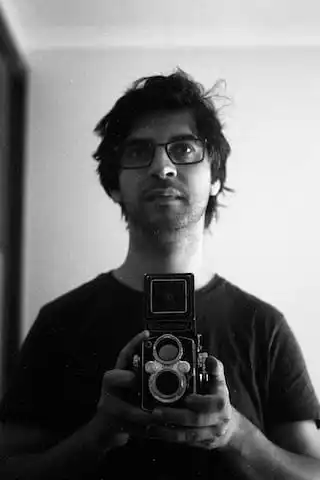 A photo of myself. The photo is in black and white, and i am taking a photo of myself, using a twin lens camera at waist level, looking towards a mirror. My hair is a bit scruffy.